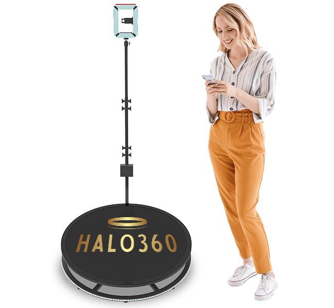Woman interacting with smartphone beside HALO360 photobooth platform, showcasing modern technology at events.