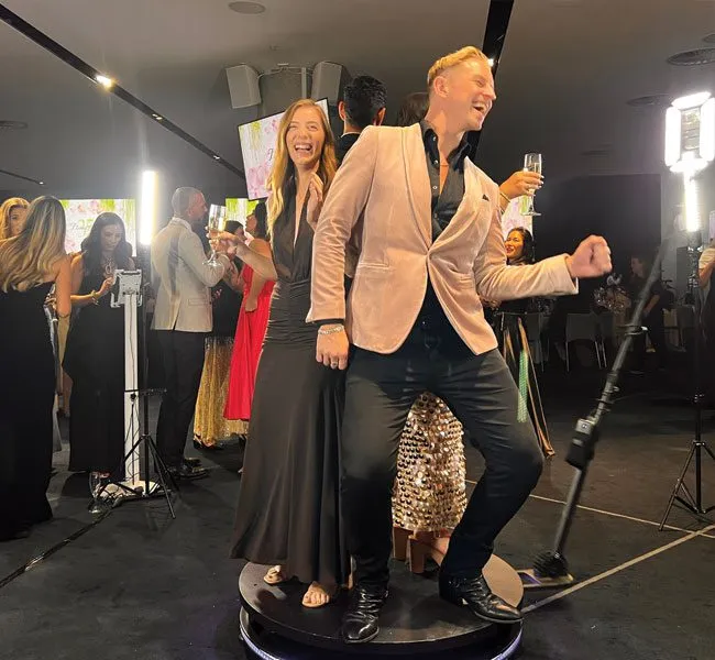 Couple enjoying 360 video booth experience at event, surrounded by guests in elegant attire, capturing shareable moments in Double Bay.