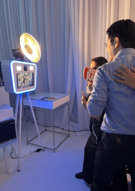 Group of people enjoying a photo session at a Premium Glam Booth with bright lighting and props, capturing memories at a private event.