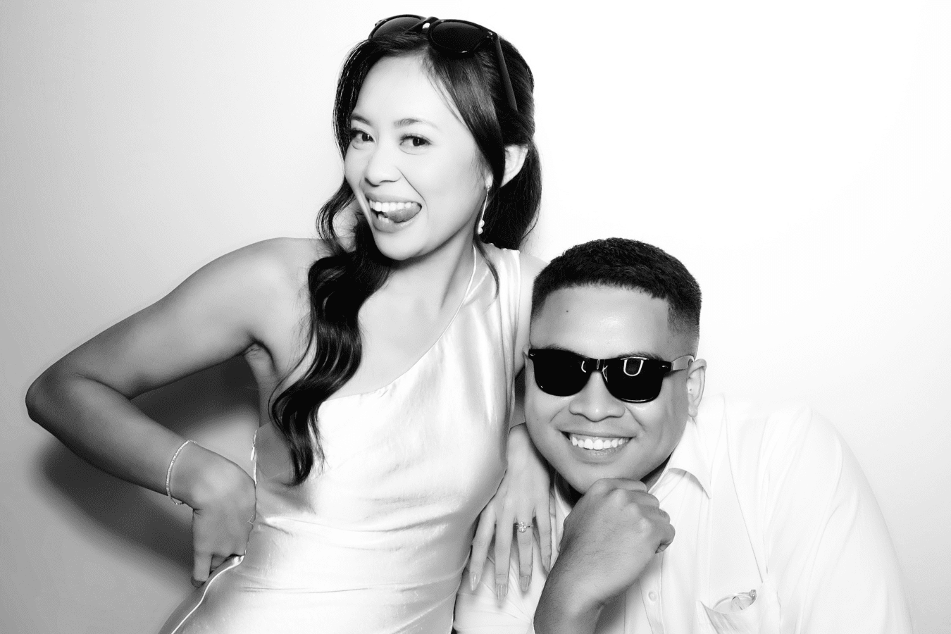 Couple posing playfully in a photo booth, showcasing joyful expressions and stylish attire, highlighting the fun and interactive experience of wedding photo booth services by Halo 360.