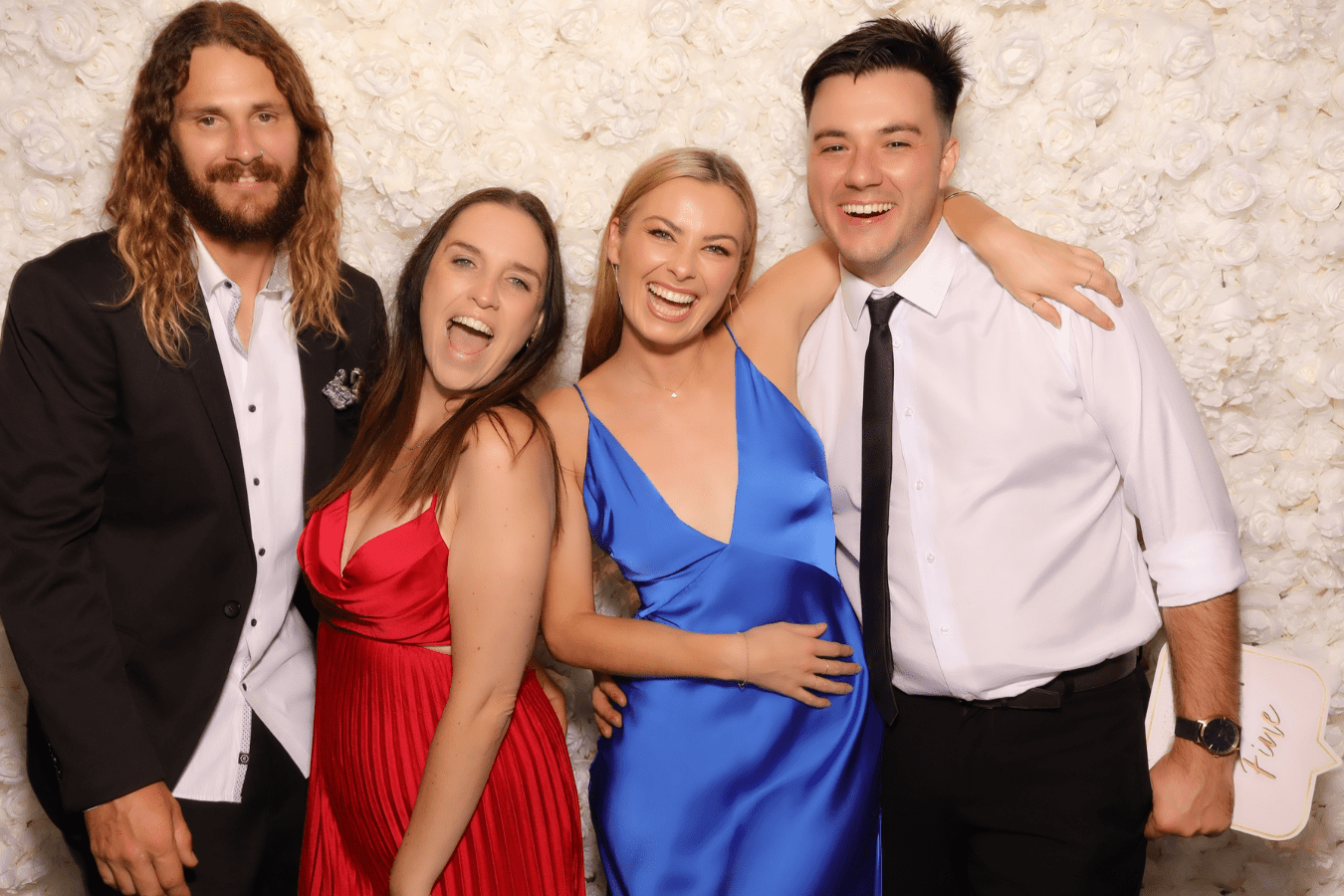 Group of four friends posing joyfully in front of a floral backdrop, showcasing a lively wedding celebration atmosphere, highlighting the fun and memorable moments captured by Halo 360's photo booth services.