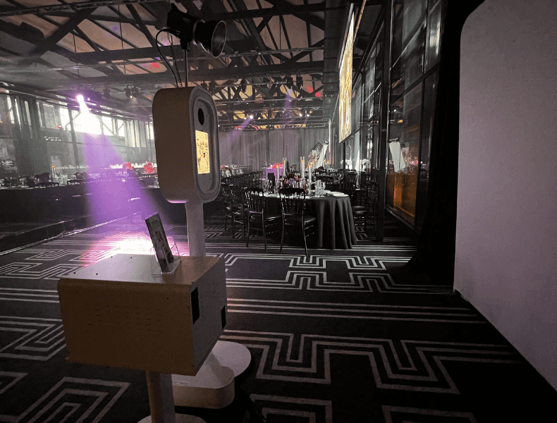 HALO360 photo booth setup in an elegant event space, featuring a sleek white booth with a touchscreen interface, surrounded by black tables and atmospheric lighting, showcasing a polished and professional presentation for weddings and celebrations.